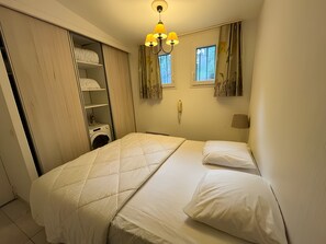 A hotel room with a bed, a wardrobe, a washing machine, and a window with curtains. - Holiday Home 'Sea View Apartment For 5 People -' with Sea View, Shared Pool and Air Conditioning (Grimaud)