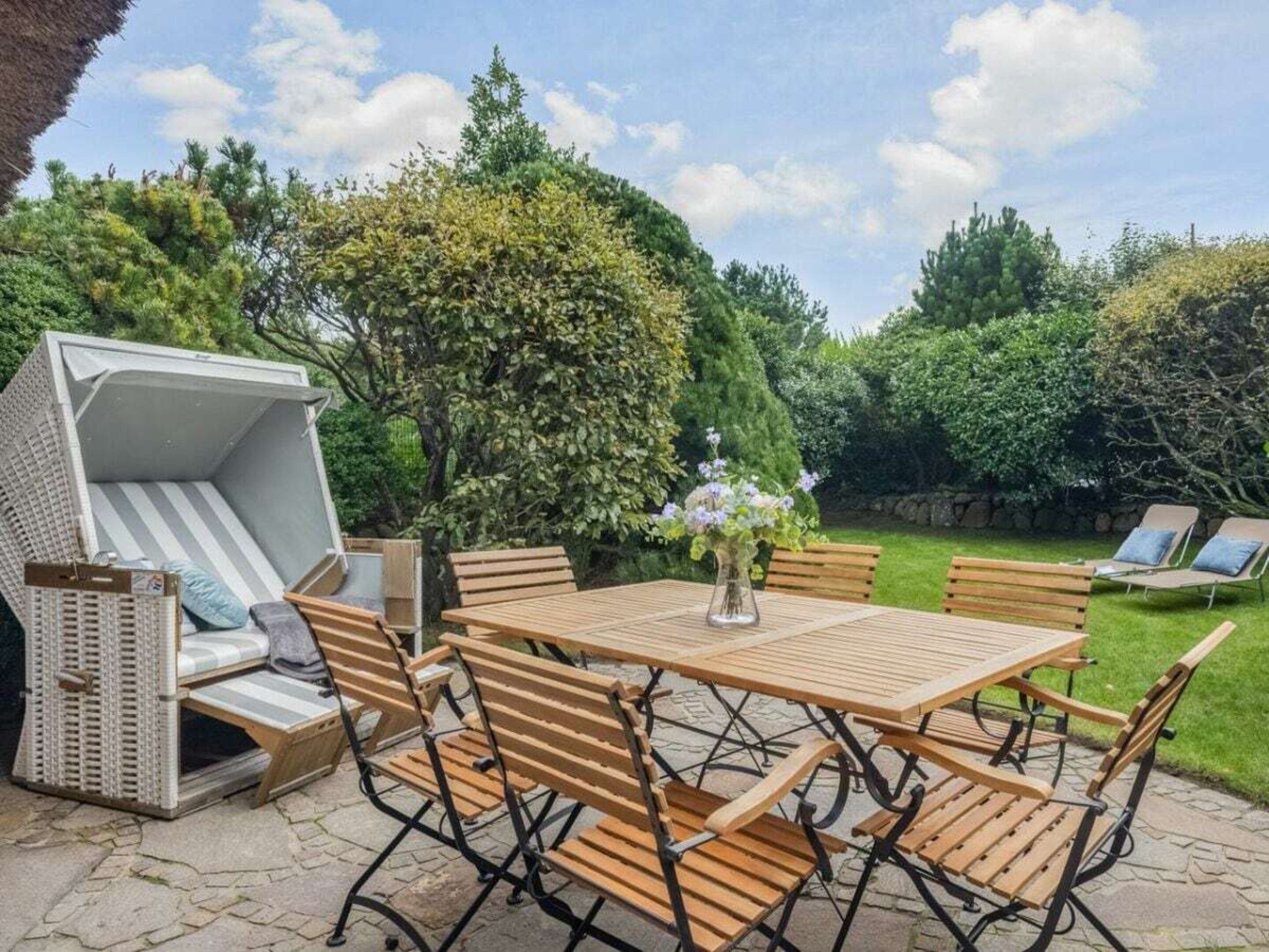 Une terrasse extérieure avec une table et des chaises en bois, un canapé en osier et un petit coin salon agrémenté de coussins.