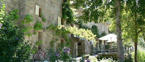 A stone building with a garden area, including a paved walkway and a bicycle.