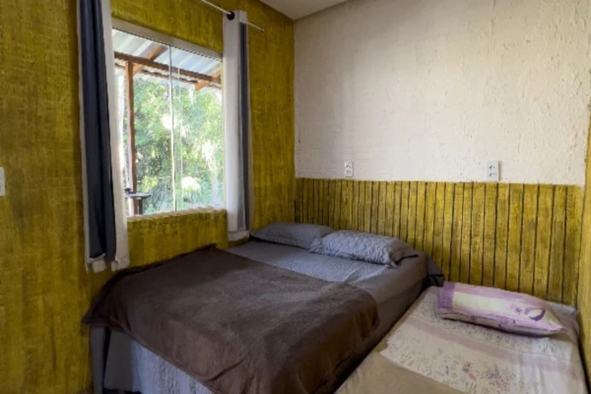 A single room with a bed, a window with curtains, and a wall with a wooden panel.