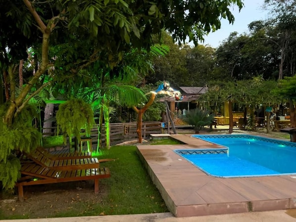 A swimming pool with a wooden deck and a bench, surrounded by lush greenery and trees. - Pousada Carijó da Serra (Santarém)