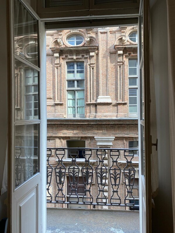 Blick durch eine Tür eines Gebäudes, das einen Balkon, aufwendige Ziegelarbeiten und mehrere Fenster zeigt.