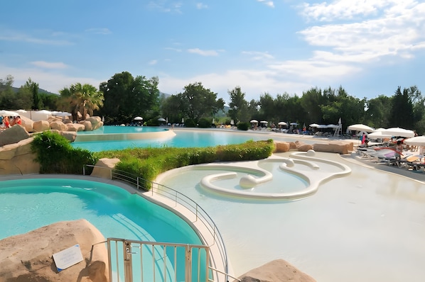 Une piscine avec une zone de vagues, entourée de chaises longues et de parasols.
