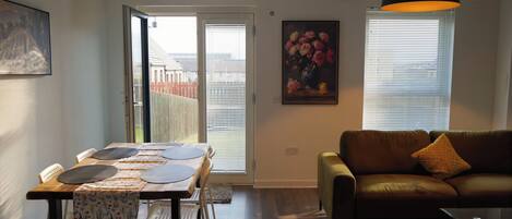A living room with a brown leather sofa, a dining table with chairs, and two pendant lights.