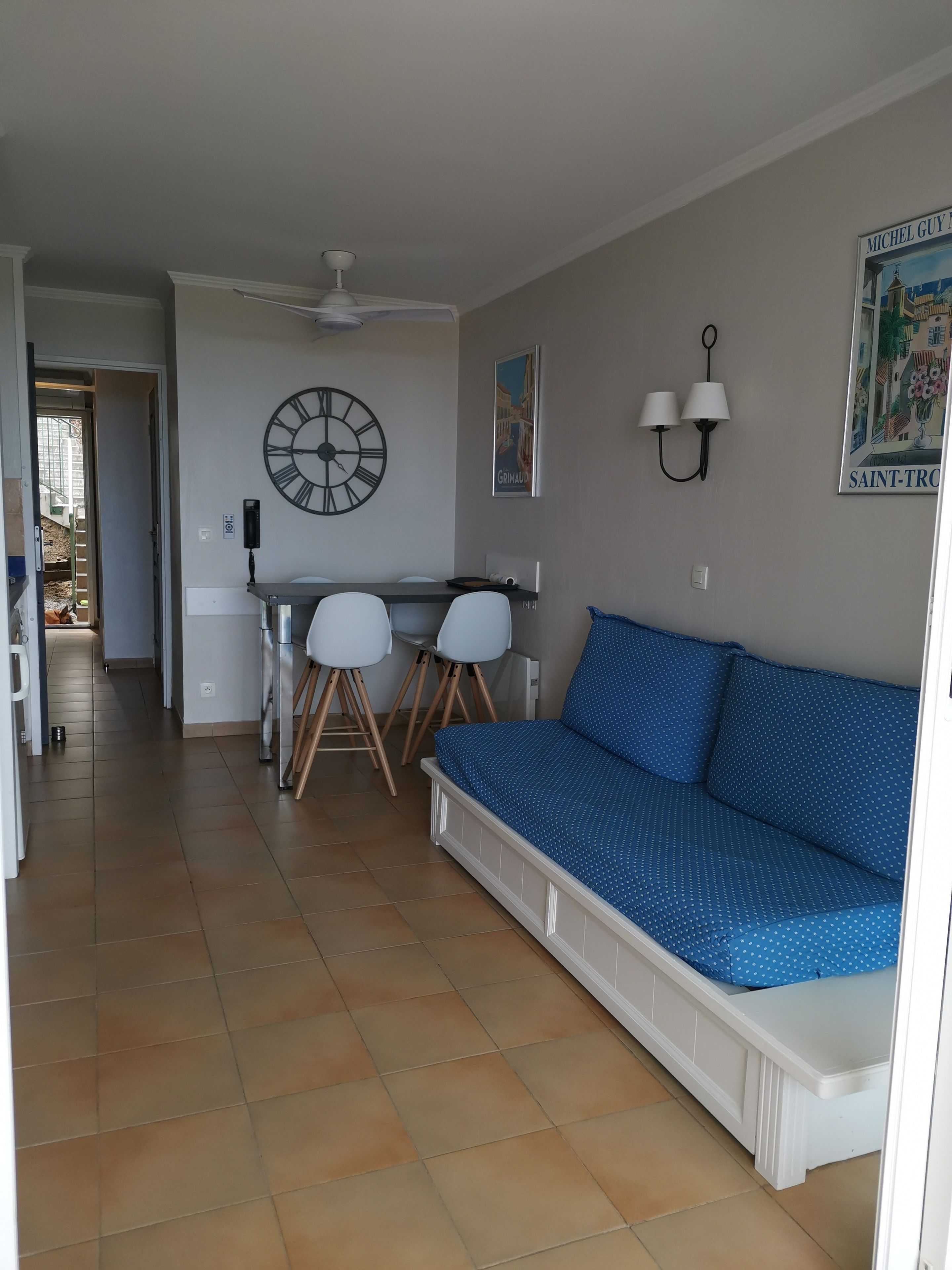 Ein Wohnzimmer mit einer Couch, einem Esstisch mit Stühlen, einer Wanduhr und einem Deckenventilator.