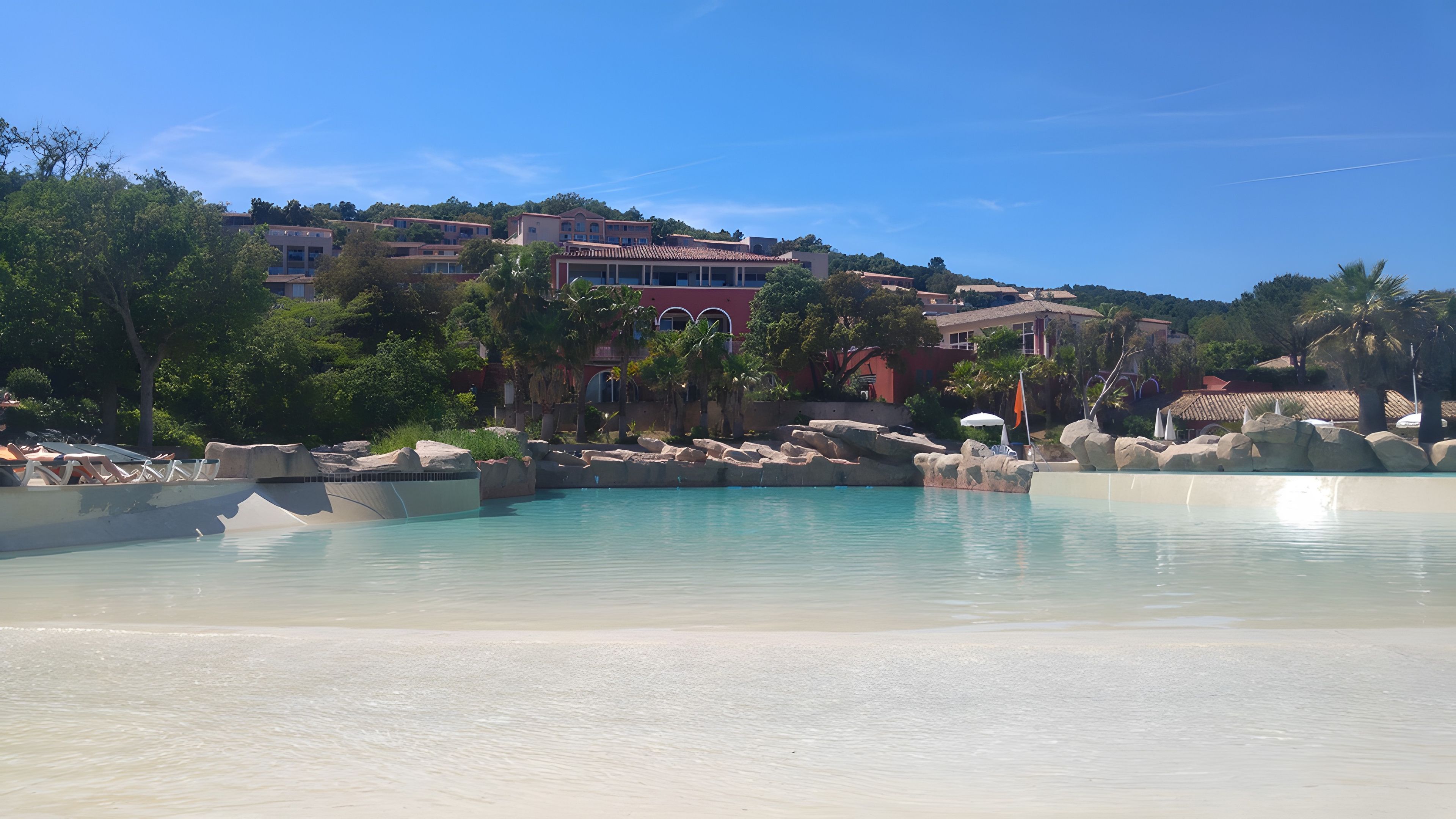 Un complexe hôtelier doté d’une piscine, de palmiers et de bâtiments en arrière-plan.