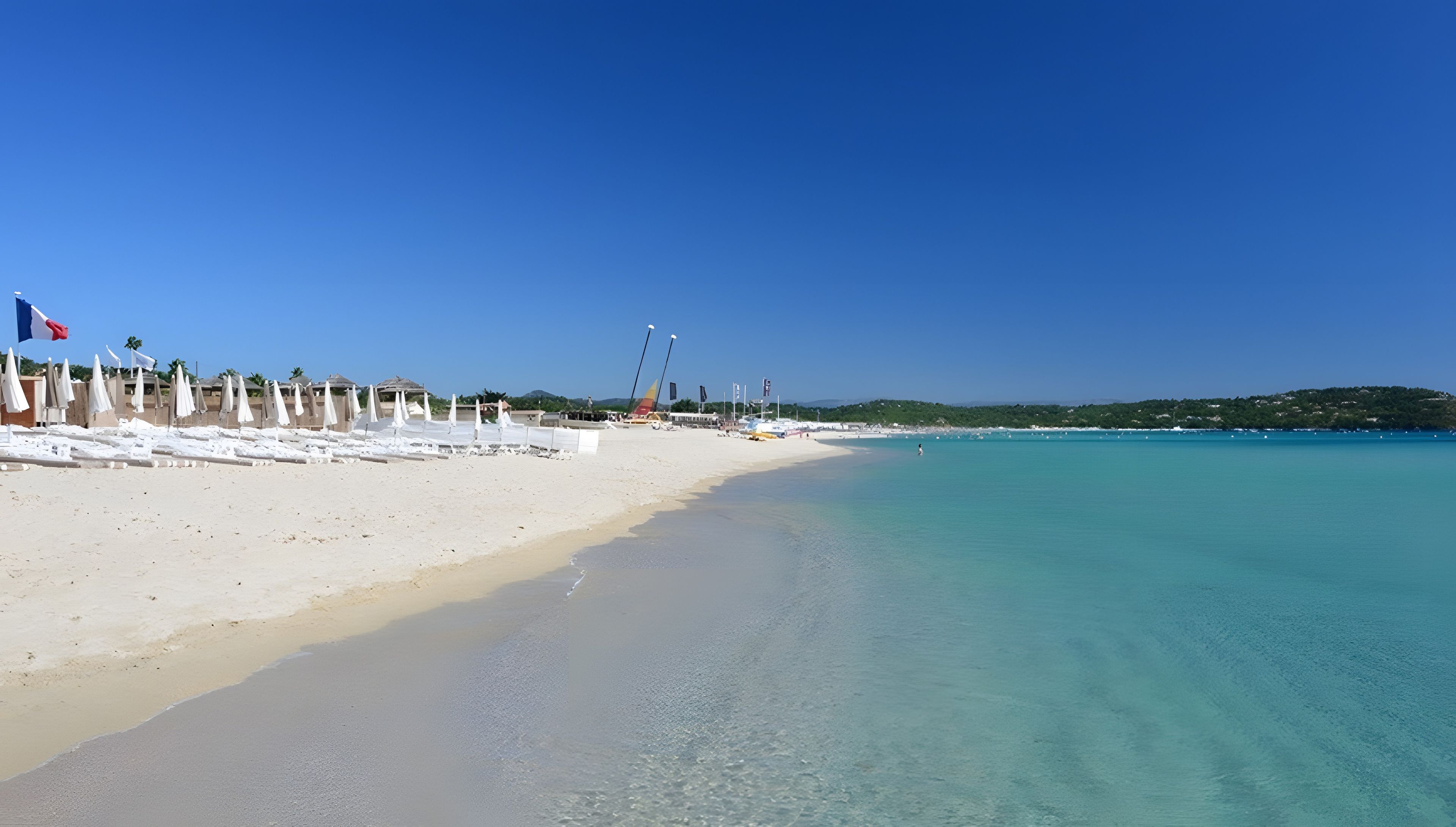 A beach with white sand, clear turquoise water, and a row of white umbrellas.