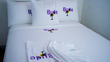 A hotel room with a bed, pillows, and a towel with the name 'Bude' and a palm tree design.