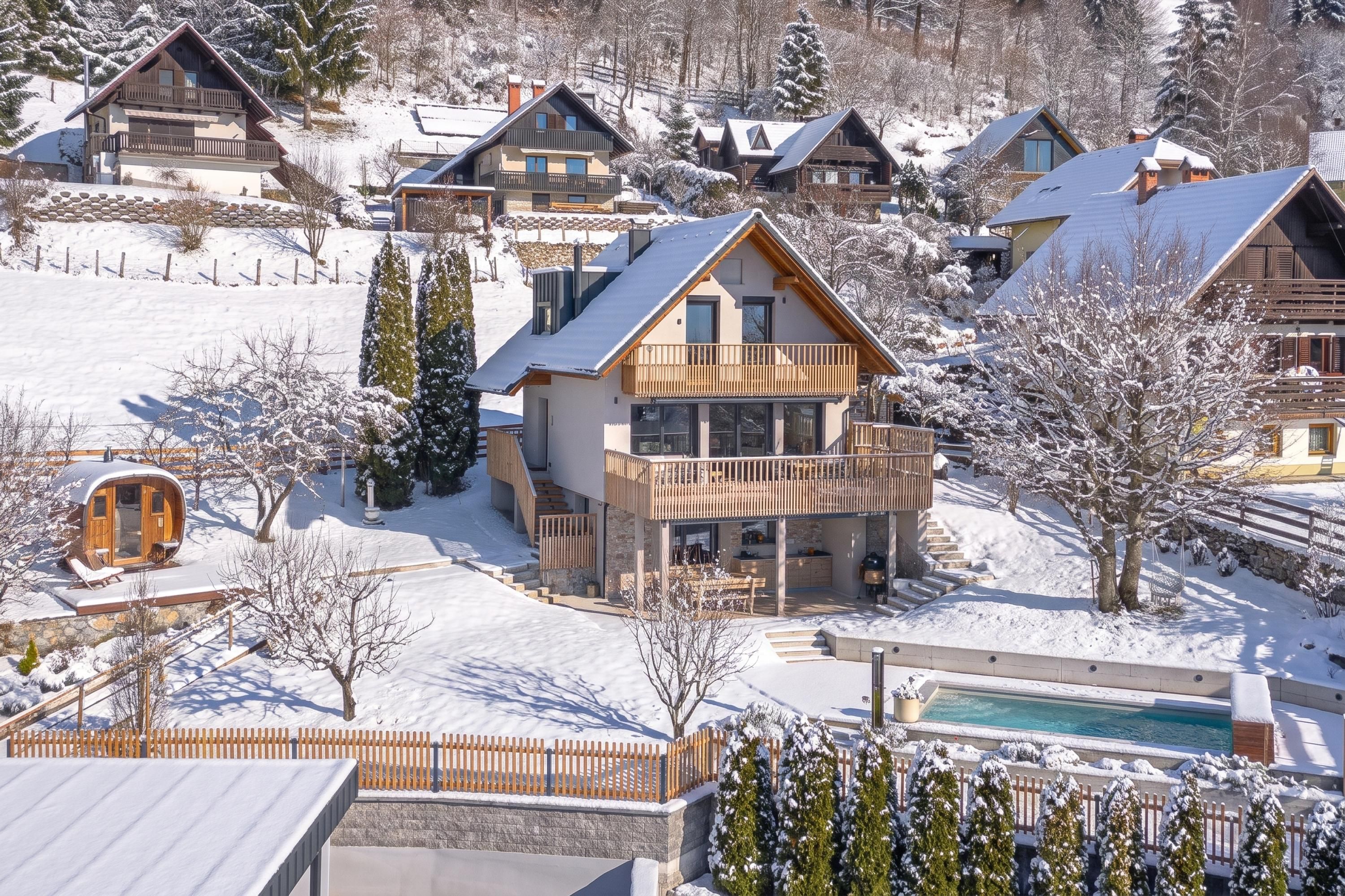 A snow-covered residential area with multiple houses, a pool, and a wooden fence.