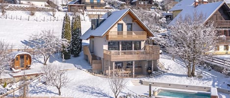 A snow-covered residential area with multiple houses, a pool, and a wooden fence.