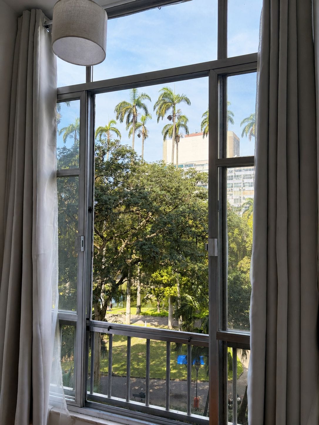 Una habitación con un ventanal, cortinas y vistas a palmeras y edificios.