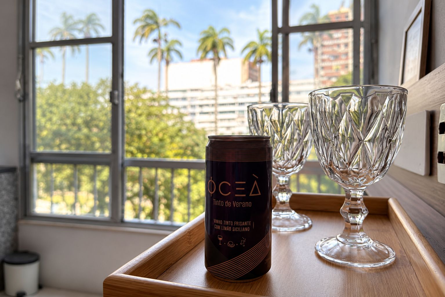 A window with a view of palm trees and buildings, a tray with a wine bottle and glasses.