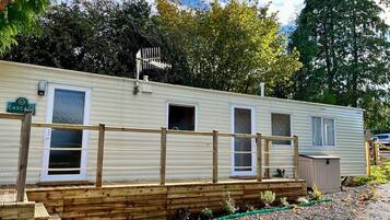 Una casa móvil con terraza de madera, un cobertizo pequeño y un camino de entrada de grava.