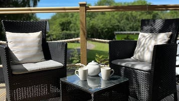 An outdoor seating area with wicker chairs and a table, a teapot, and cups on the table.