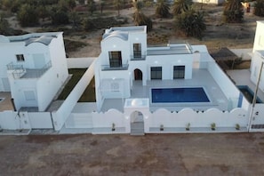 Ein modernes, weißes Gebäude mit Pool, überdachter Terrasse und angelegtem Garten.