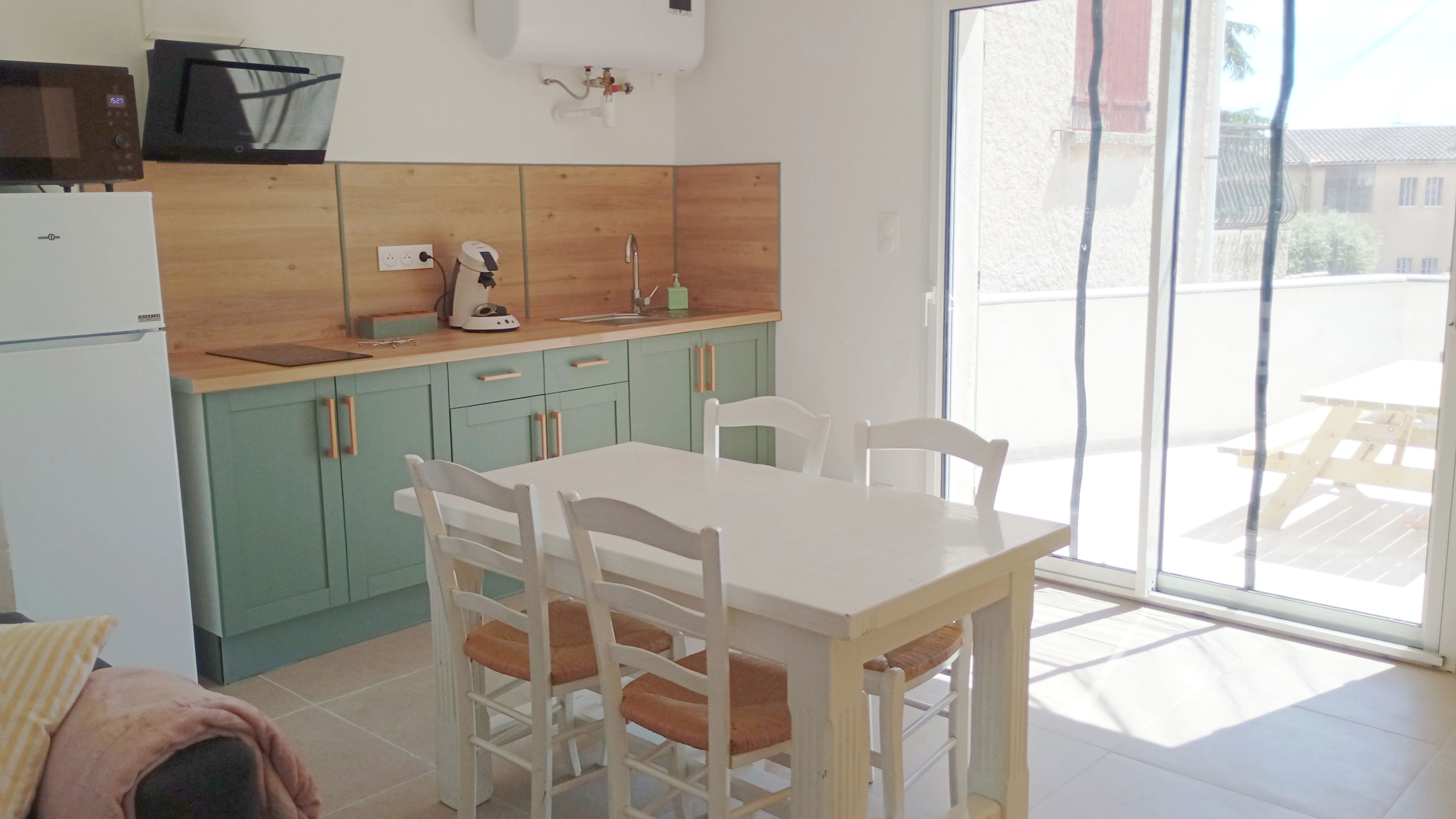 Een keuken met een eettafel en stoelen, een magnetron, een waterkoker en een spoelbak.