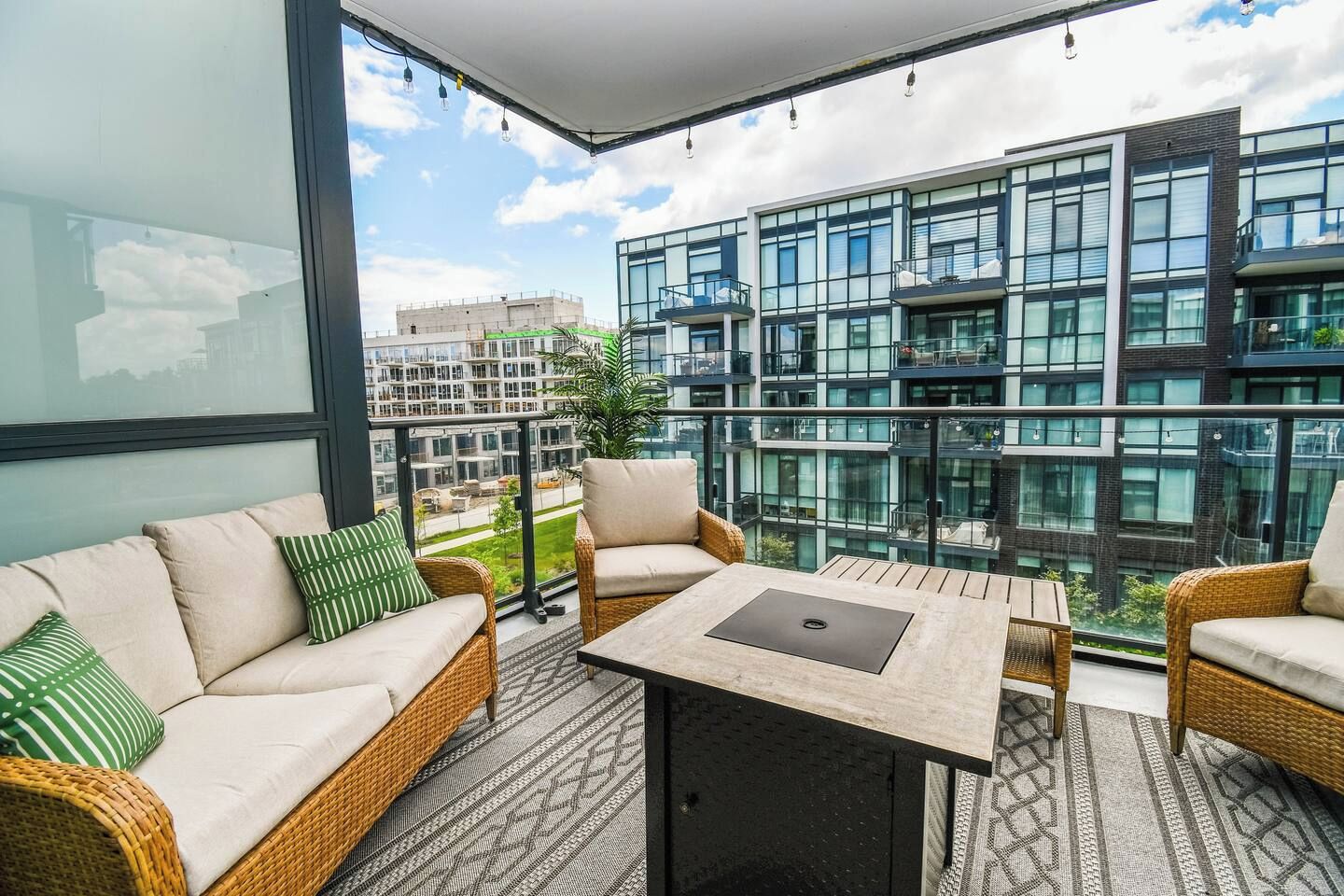 Un balcon doté de meubles en osier, d’une table et offrant une vue sur des immeubles modernes.