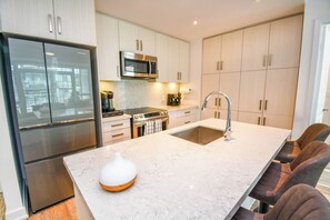 A modern kitchen with a stainless steel refrigerator, a microwave, a sink, and a bar area with seating. - Luxury 2BD Condo Friday Harbour Resort (Innisfil)