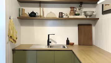 Una cocina con un lavamanos, armarios verdes y diversos utensilios de cocina en estantes.