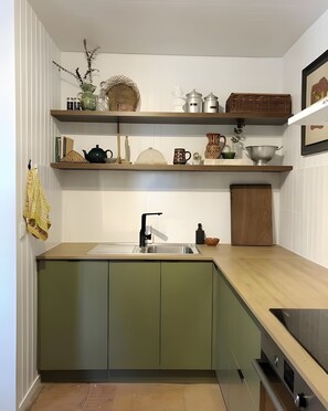 Una cocina con un lavamanos, armarios verdes y diversos utensilios de cocina en estantes.