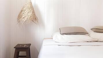 A bedroom with a bed, pillows, a small wooden stool, and a woven lamp.