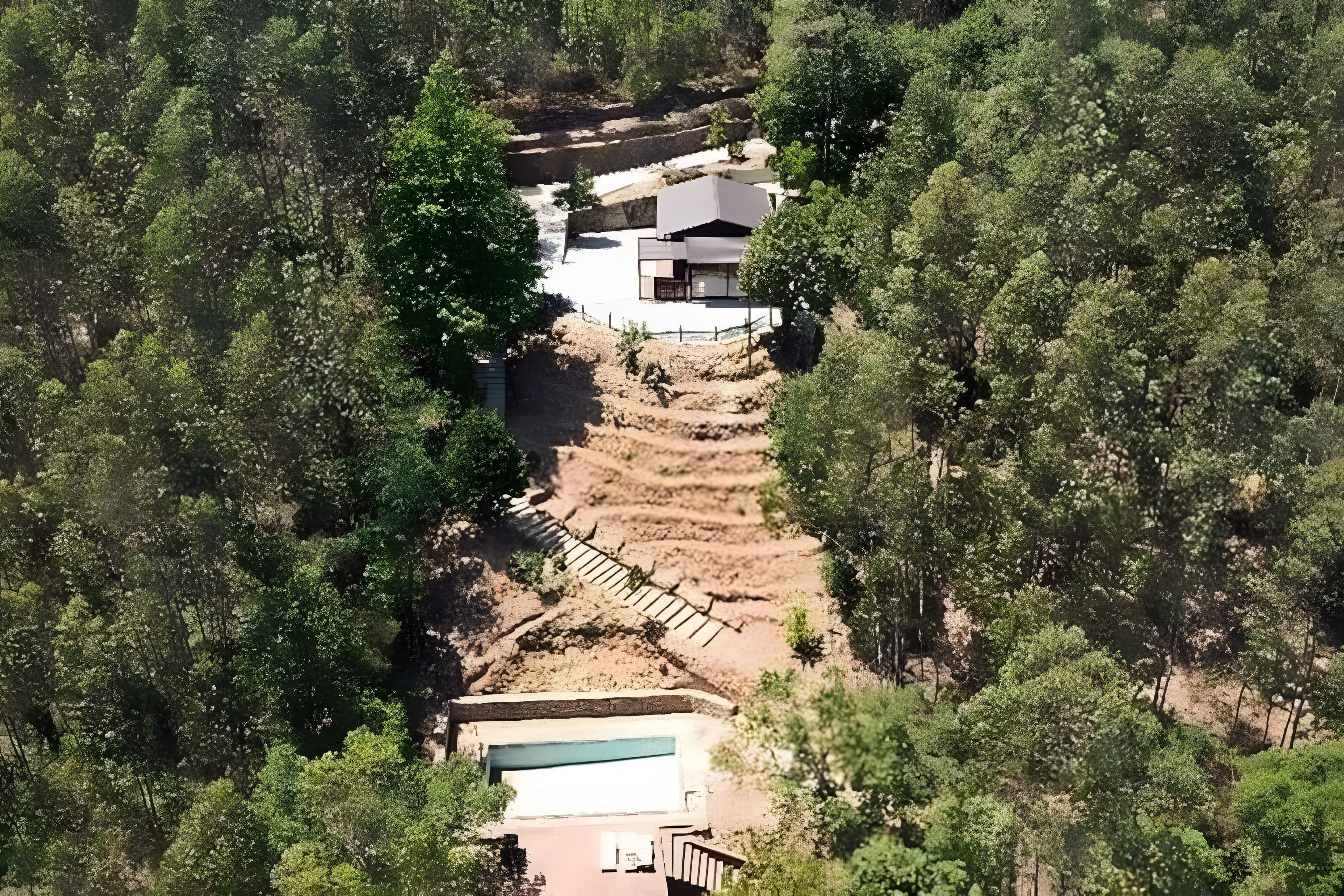 Una propietat situada en un turó amb piscina, escala i edifici amb teulada plana.