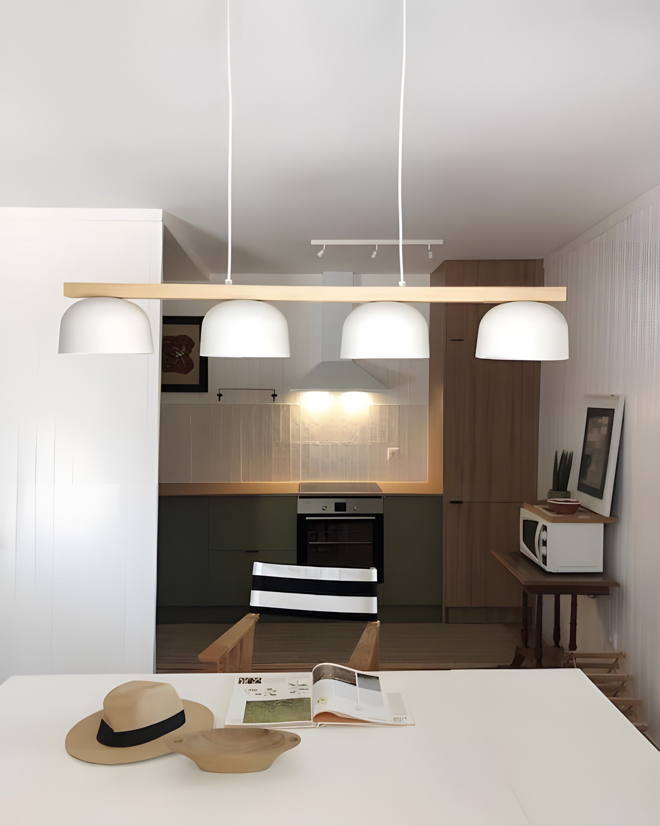 Una cocina moderna con una isla central, luces colgantes y un microondas sobre una mesita auxiliar.