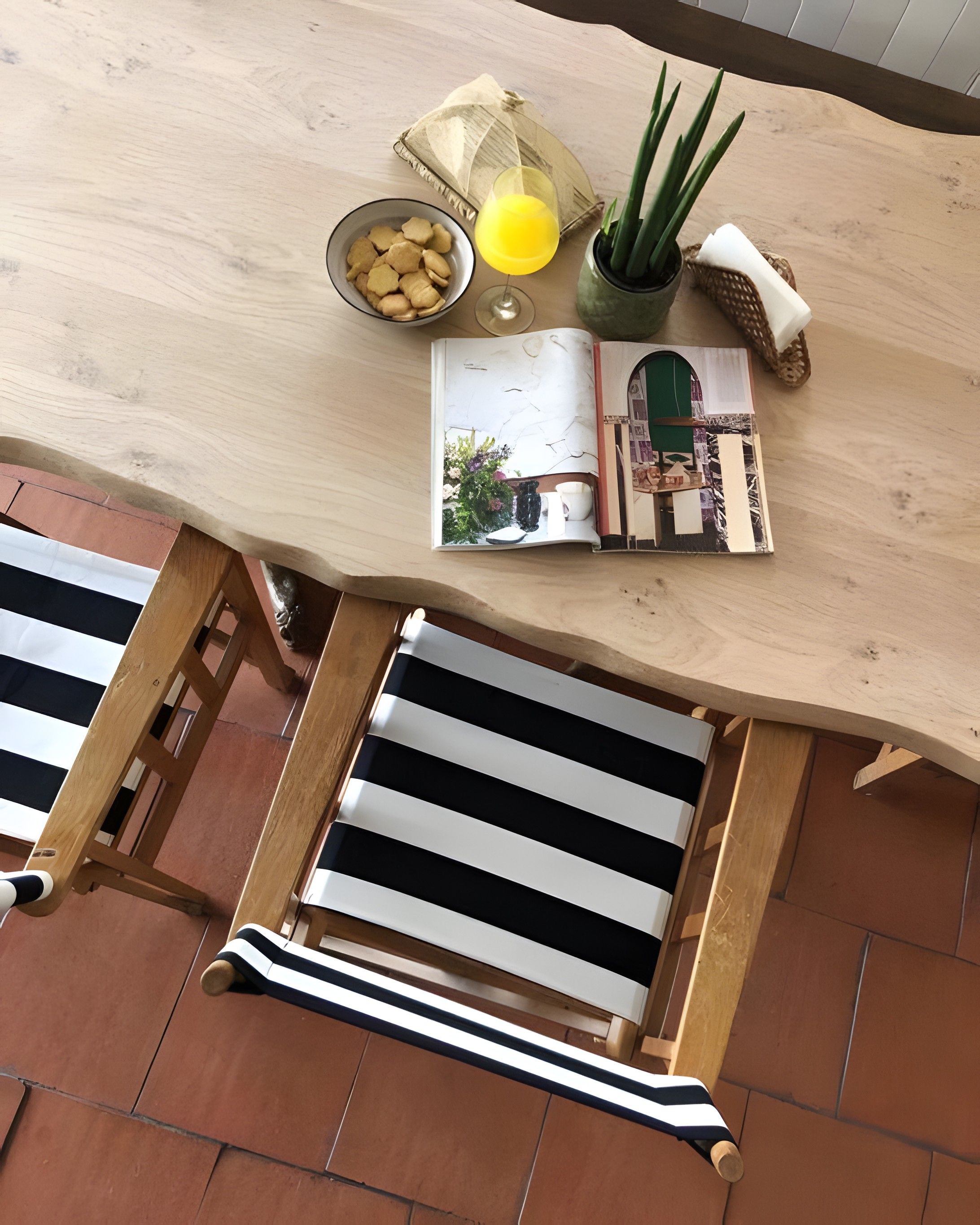 Una mesa de madera con una revista, un cuenco de bocadillos, una planta en maceta y una vela.