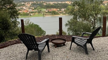 An outdoor seating area with two chairs and a small table, overlooking a lake and a distant town.