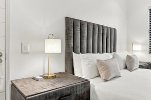 A hotel room with a bed, two bedside lamps, a nightstand, and a window with blinds. - York | Relaxed 1BR with Ocean Outlook (Umhlanga)