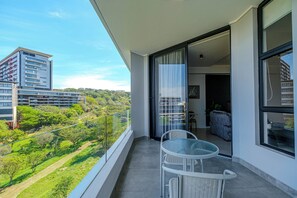 Varanda com mesa e cadeiras, vista para uma paisagem verde e o horizonte urbano.