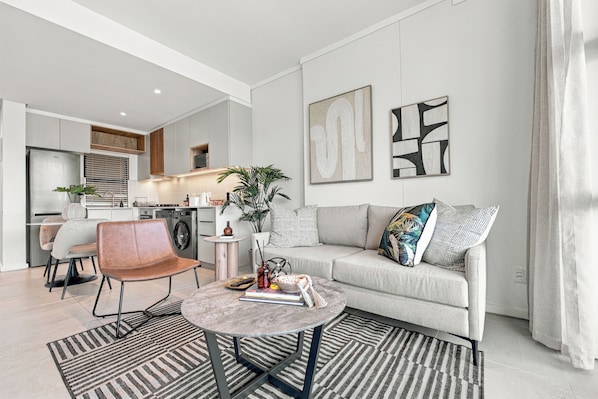 Uma sala de estar moderna com um sofá cinza, uma mesa de centro e um espaço de jantar com uma cadeira e mesa.