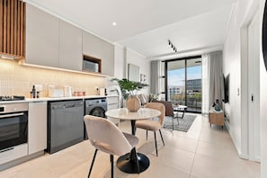 Cozinha moderna com eletrodomésticos embutidos, área de jantar com mesa e cadeiras redondas, e uma grande janela com vista para edifícios.