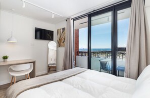 Ein Hotelzimmer mit Bett, Schreibtisch, Stuhl, Fernseher und einem Balkon mit Blick.