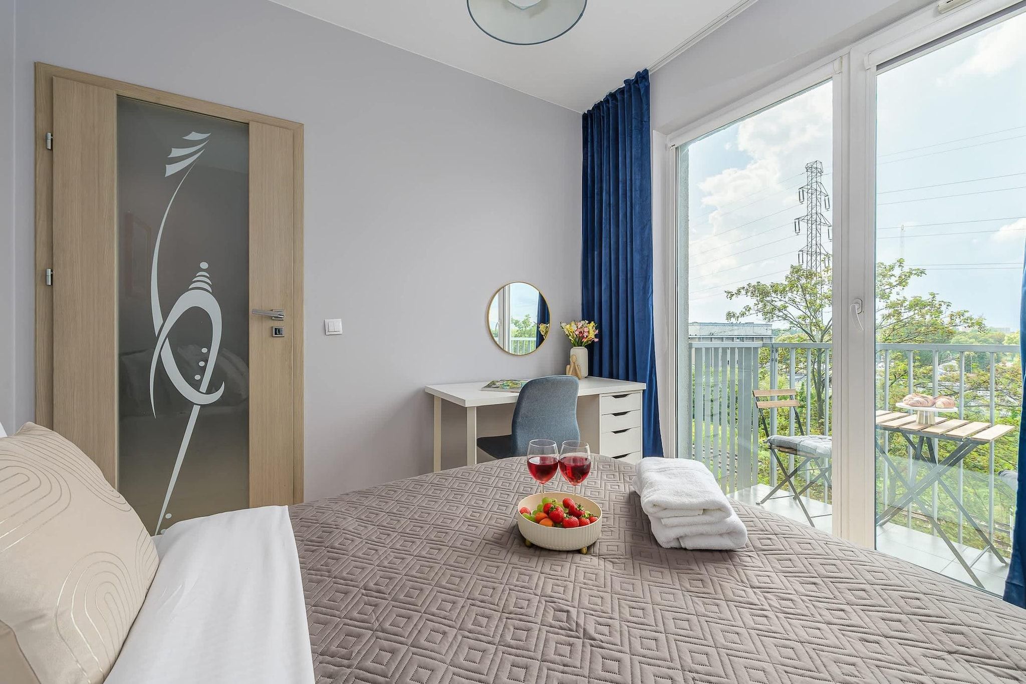 A hotel room with a bed, a desk, a chair, a balcony with a view, and a window.
