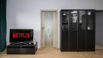 Una stanza con una televisione che mostra 'NETFLIX', un mobile in legno con ante in vetro e una porta con pannello traslucido.