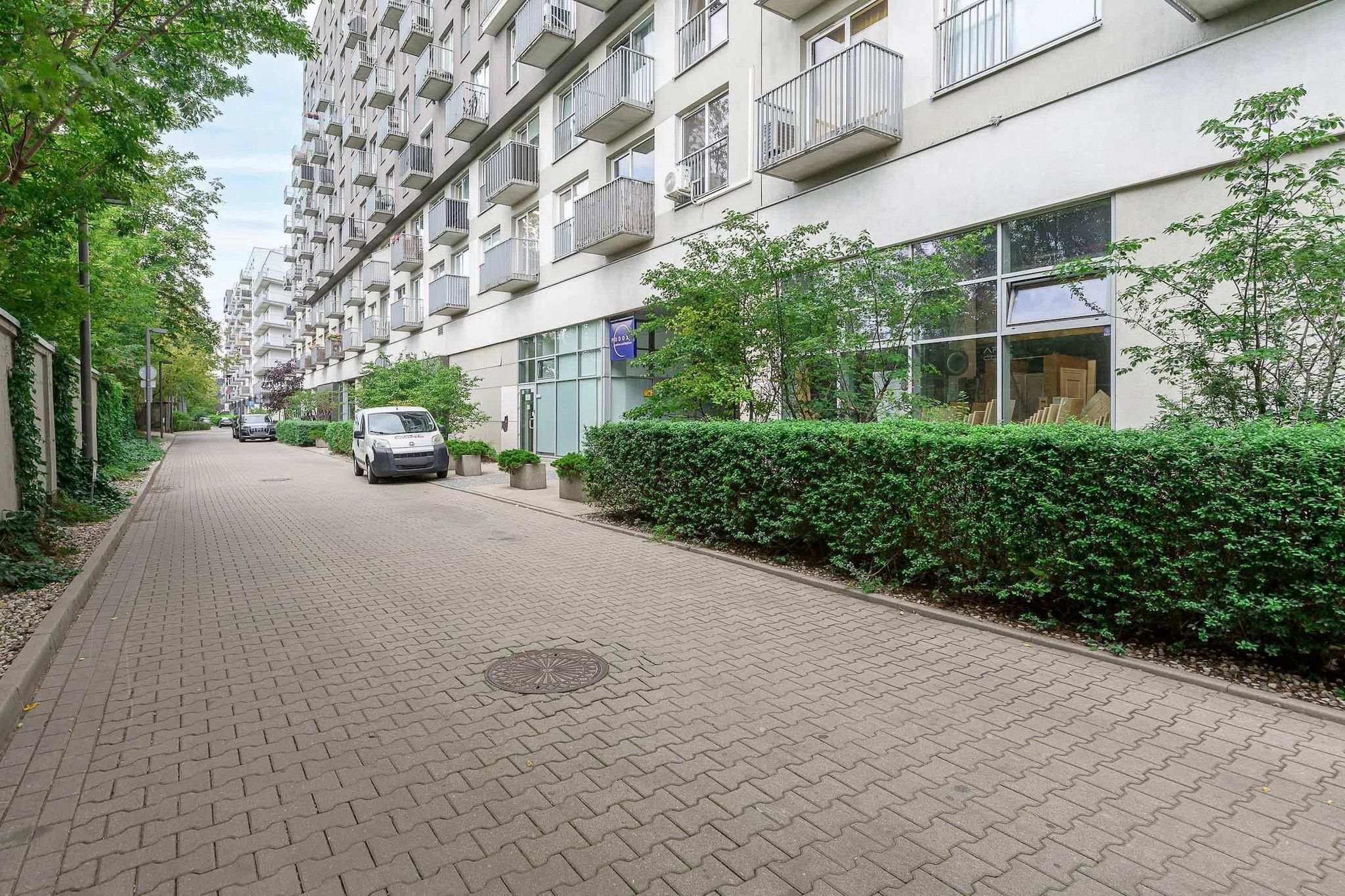 A residential building with multiple balconies, a paved pathway, and a parked car.