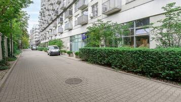 A residential building with multiple balconies, a paved pathway, and a parked car.
