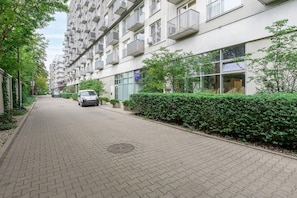 A residential building with multiple balconies, a paved pathway, and a parked car. - Apartment near Młynów Metro (Warszawa)