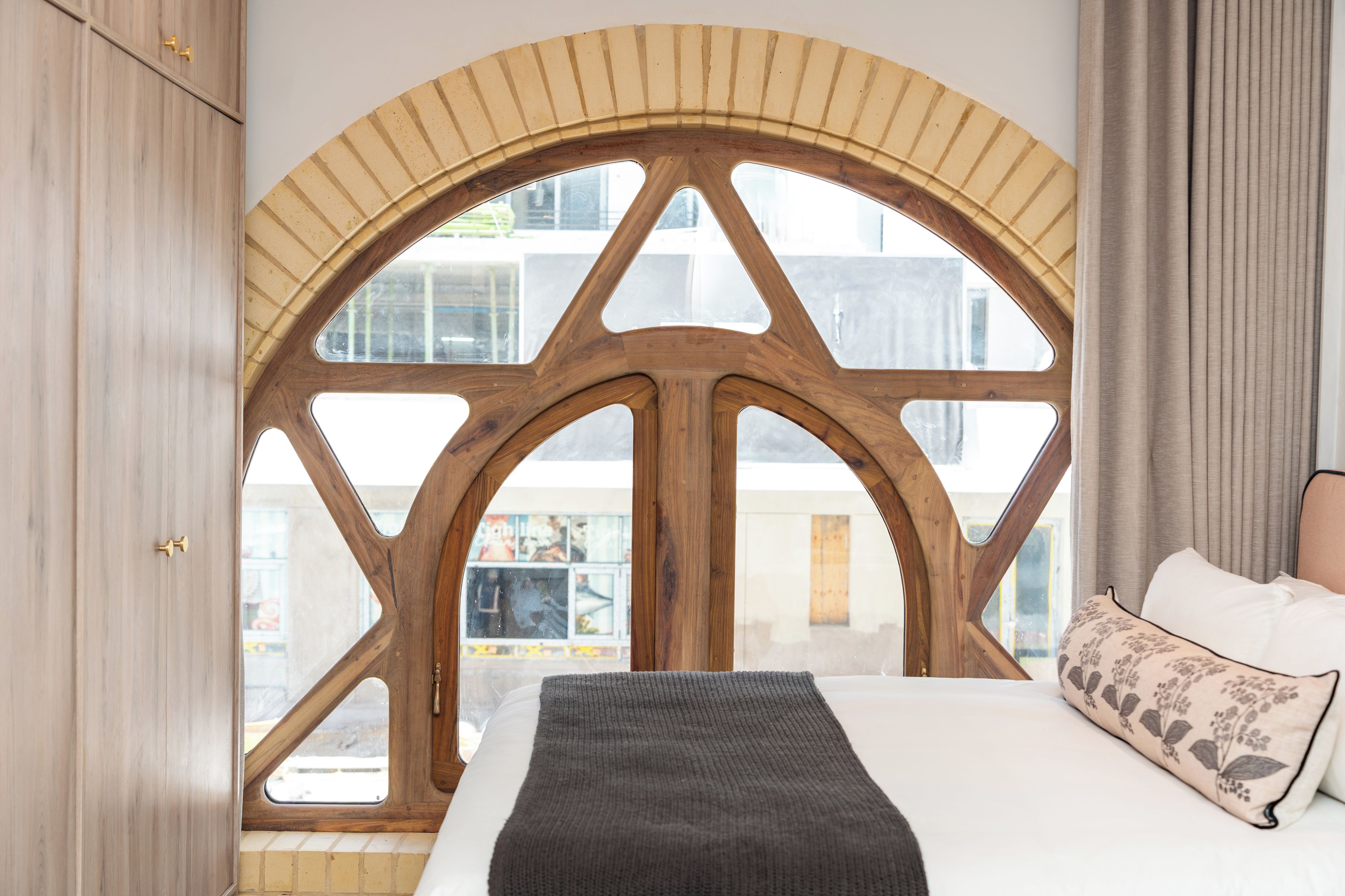 A bedroom with a large arched window, a bed with a white headboard, and a grey throw blanket.