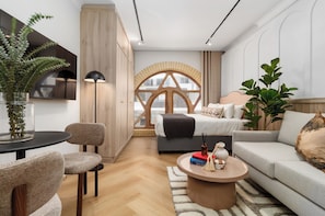 Ein modernes Wohnzimmer mit einer Couch, einem Couchtisch, einem Sessel, einem Fernseher und einem großen Fenster mit Holzrahmen.