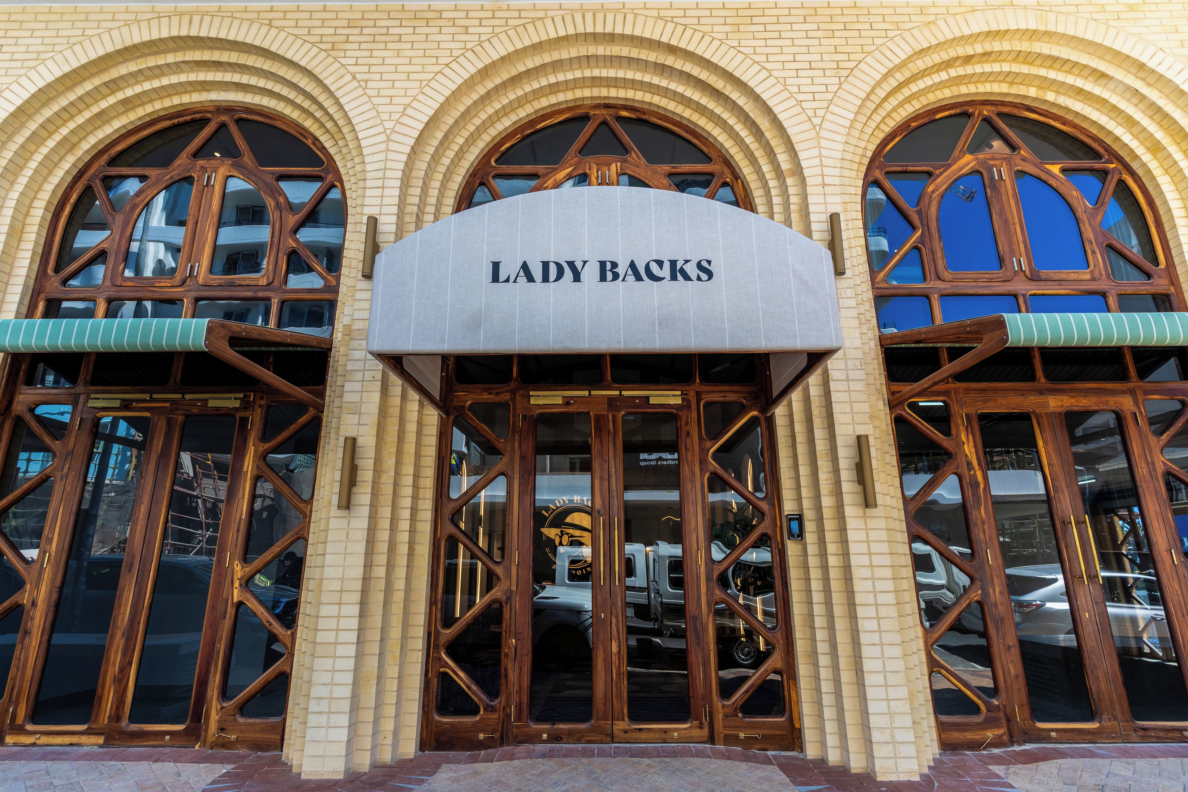 A storefront with the sign 'LADY BACKS' above the entrance, featuring large arched windows and a brick facade.