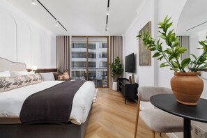 Ein modernes Hotelzimmer mit Bett, Schreibtisch, Stuhl, Fernseher und einem Balkon mit Blick auf das Gebäude.