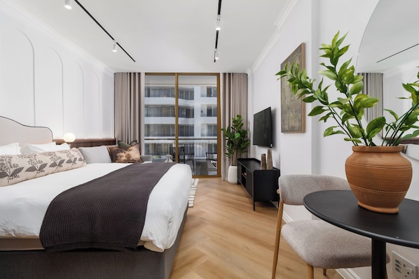 Une chambre d’hôtel moderne équipée d’un lit, d’un bureau, d’une chaise, d’une télévision et d’un balcon offrant une vue sur l’immeuble.
