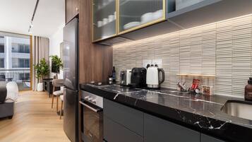 A modern kitchen with a black marble countertop, stainless steel appliances, and a view of the city through large windows.