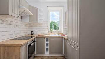 A compact kitchen with a built-in oven, a window with a view of greenery, and a wooden countertop.