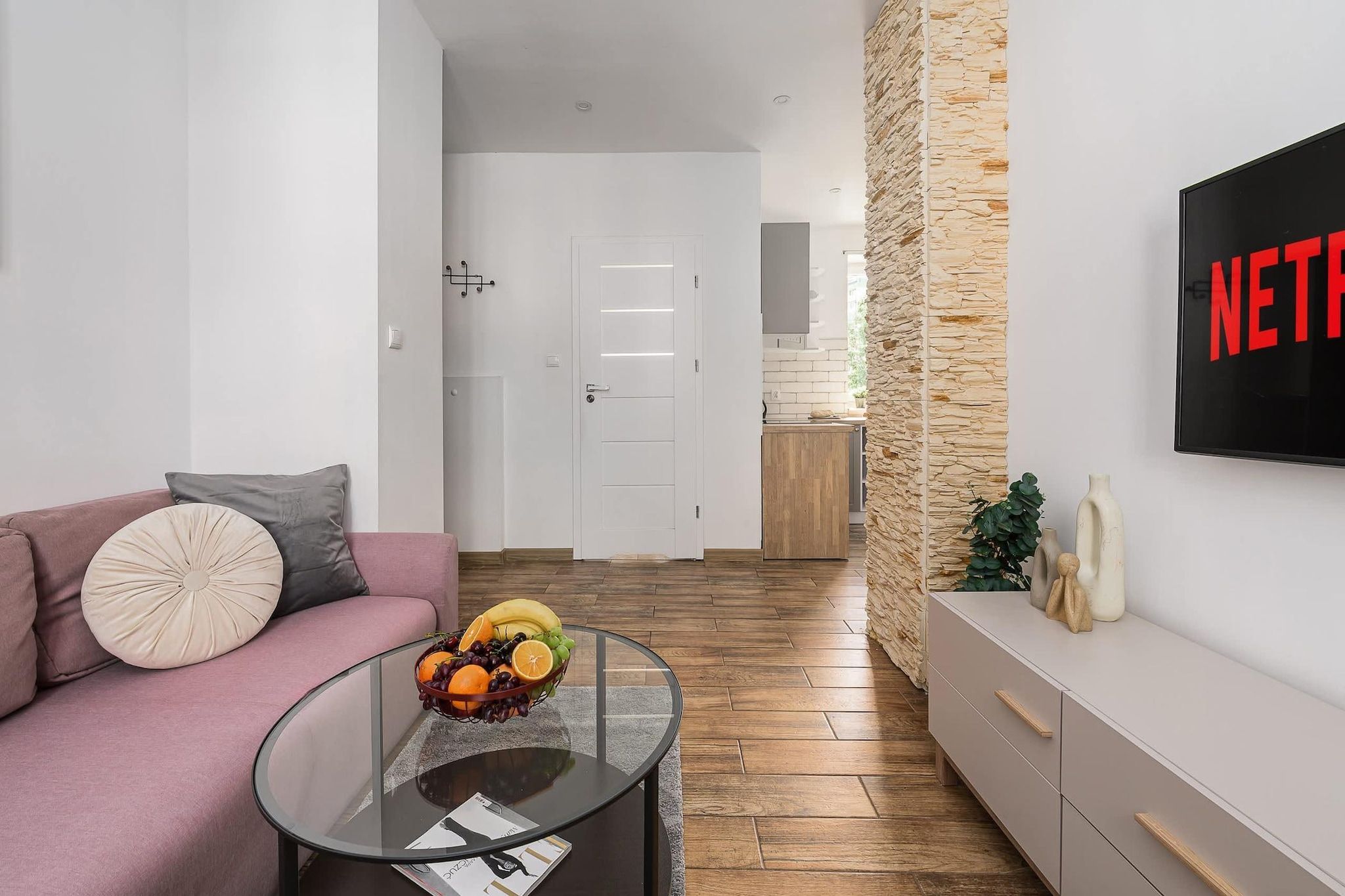 A modern living room with a sofa, coffee table, fruit bowl, and a TV mounted on the wall.