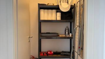 A narrow hallway with a metal shelving unit containing towels, a fire extinguisher, and a black suitcase.