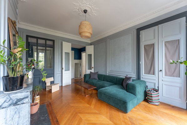 Ein geräumiges Wohnzimmer mit einem grünen Sofa, Holzboden und einem großen Spiegel.