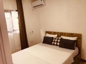 Une chambre d’hôtel avec un lit, une tête de lit en bois et un appareil de climatisation fixé au mur.